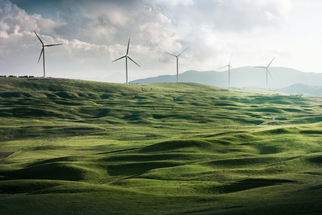 green energy - electricity generating windmills in a green pasture. Mountains in the background